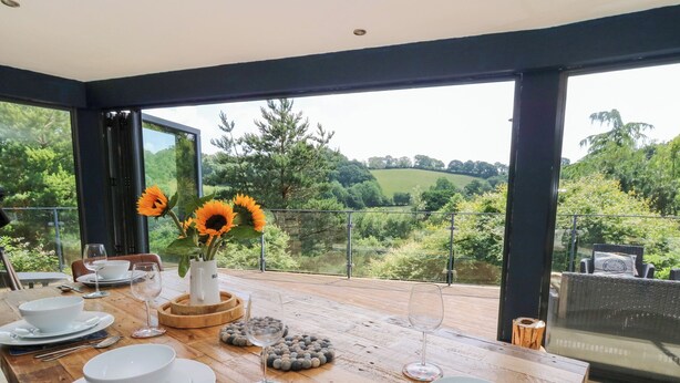 A dining table set with white plates, bowls, and cutlery, with a vase of sunflowers and a pitcher on the table. - The Old Barn (Lampeter)