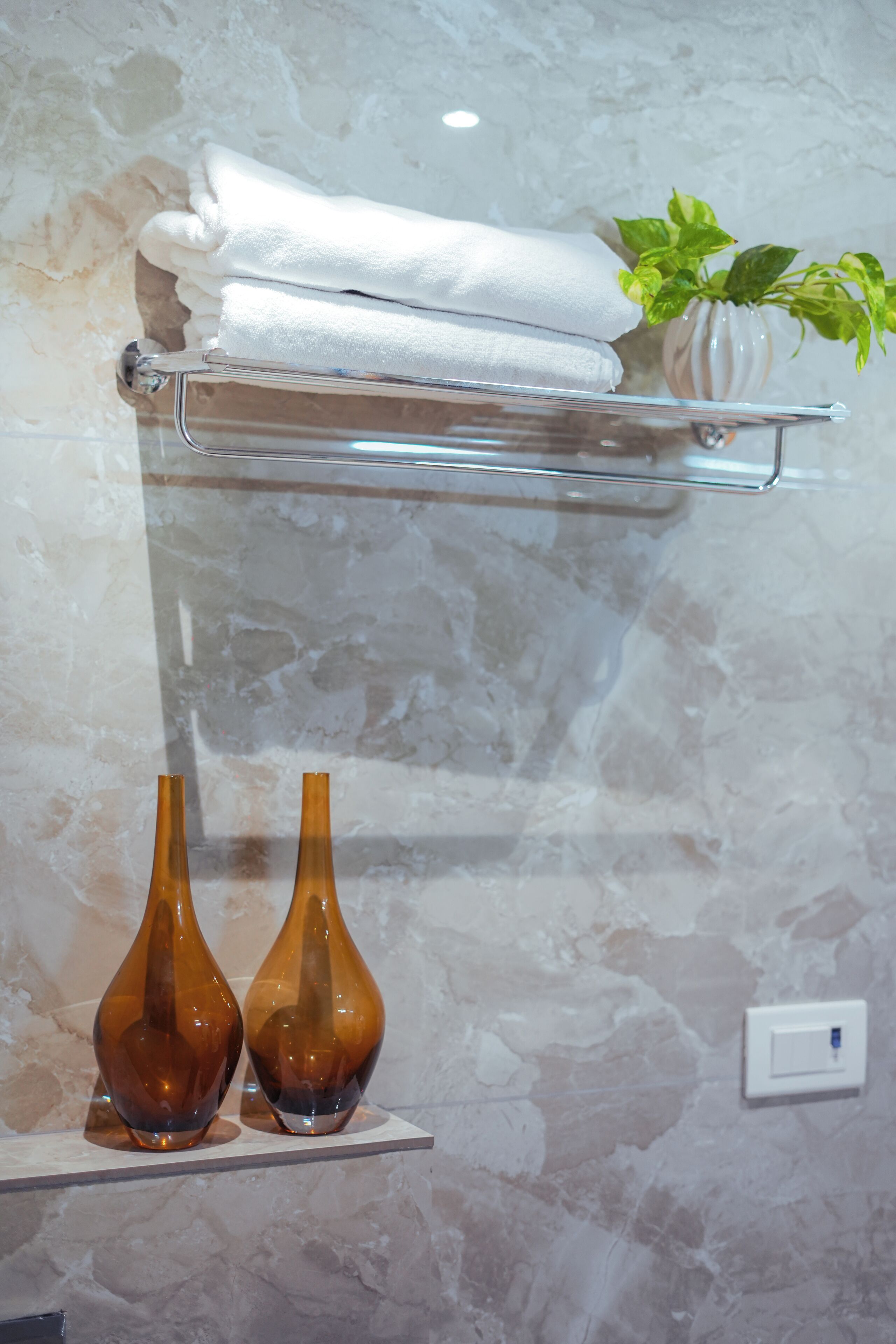 A bathroom with a marble wall, a towel rack with folded towels, two decorative vases, and a potted plant.