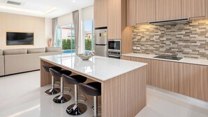 Una cocina moderna con una isla central, taburetes de bar, electrodomésticos integrados y vistas al exterior.