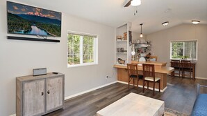 A spacious living area with a large window, a dining table, and a kitchen area with a bar.