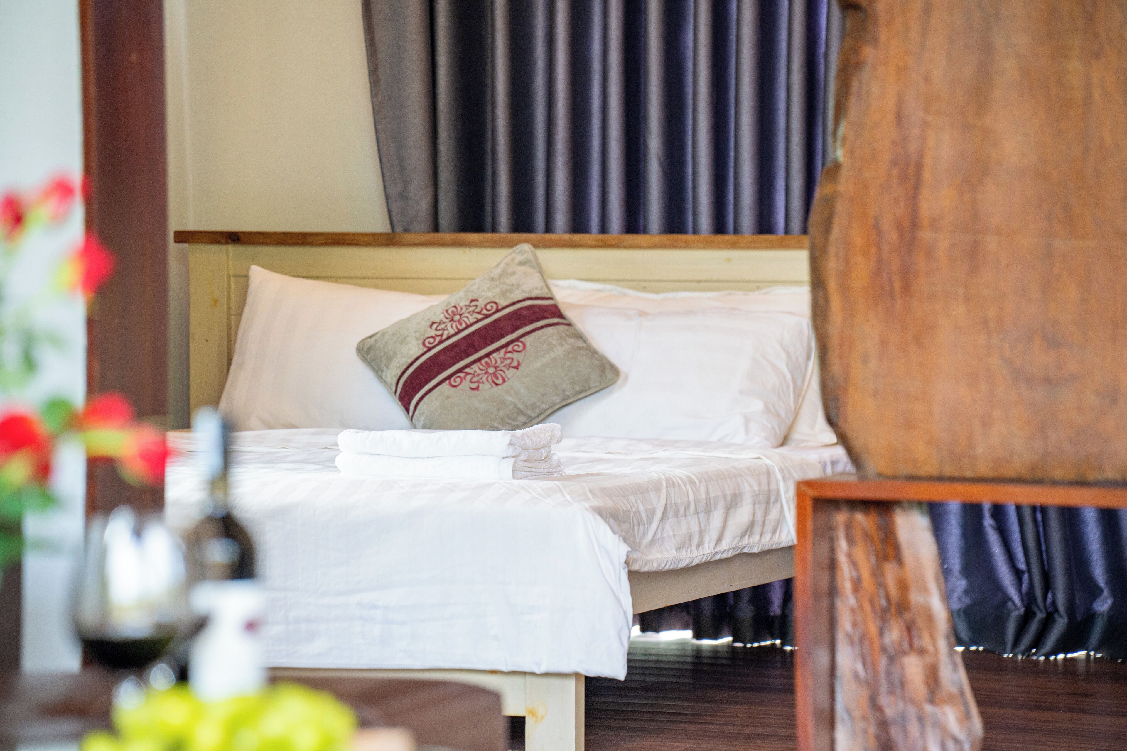 A neatly made bed with white linens and decorative pillows, a wooden headboard, and a dark curtain backdrop.