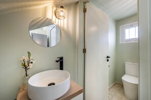 A bathroom with a round white sink, a mirror, a small vase with flowers, and a toilet. - Laranca Oneiro Seaside Villa (Pervolia)