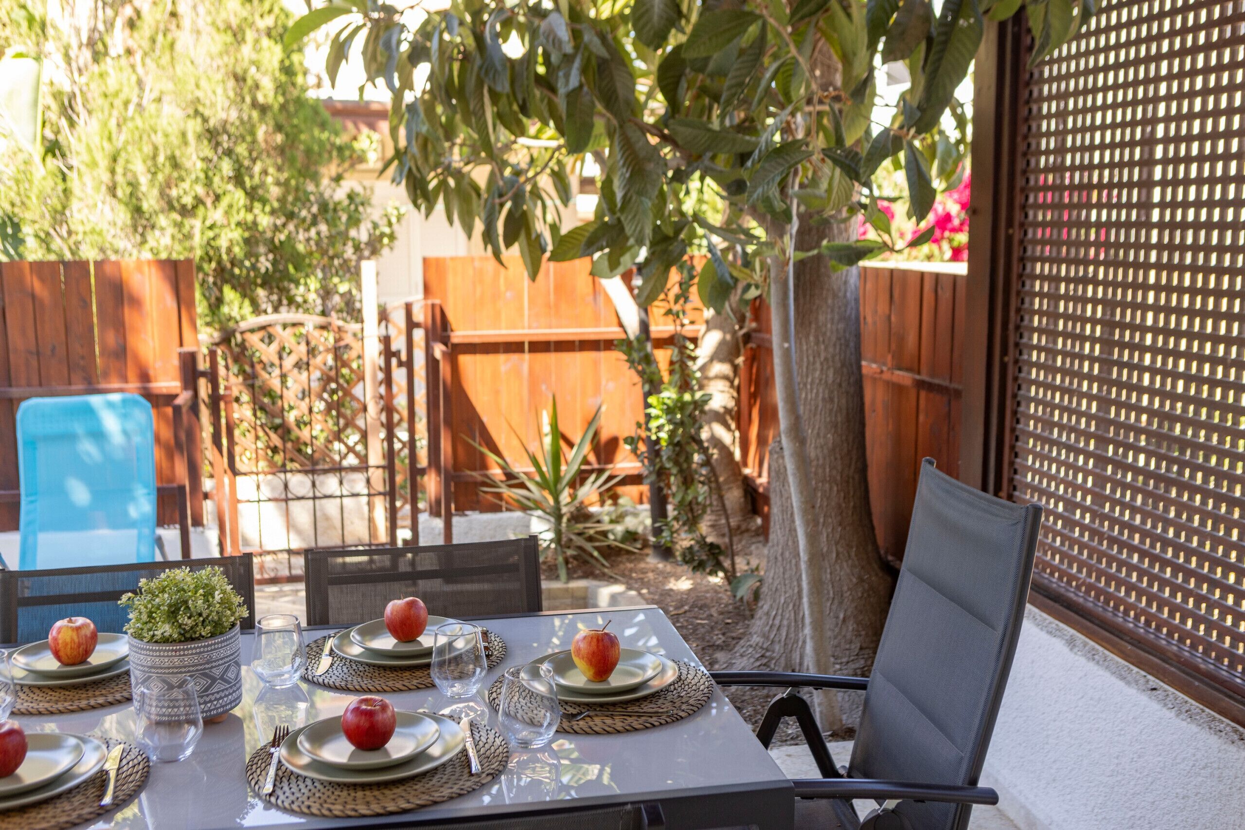 An outdoor dining area with a table set for four, surrounded by chairs, a potted plant, and a wooden fence.
