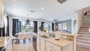 A modern kitchen with granite countertops, white cabinetry, and a dining area with a table and chairs. - 6BR Resort Villa Near Disney | Private Pool 2584 (Kissimmee)