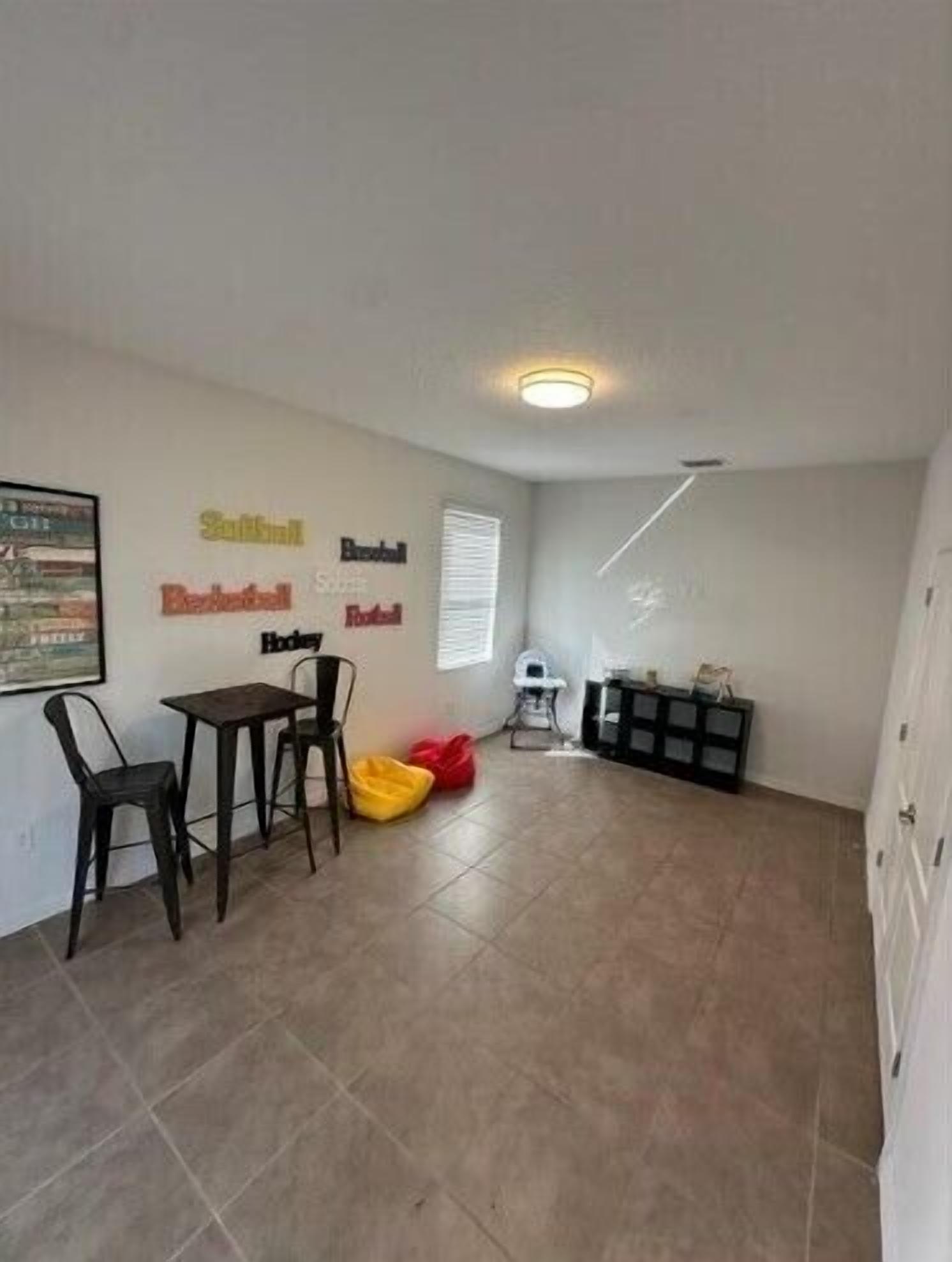 A room with a tiled floor, a small table with chairs, a red bag, and a white cabinet.