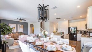 A modern kitchen with white cabinets, a black refrigerator, and a dining area with a wooden table set for six. - 6BR Resort Villa Near Disney | Private Pool 2584 (Kissimmee)