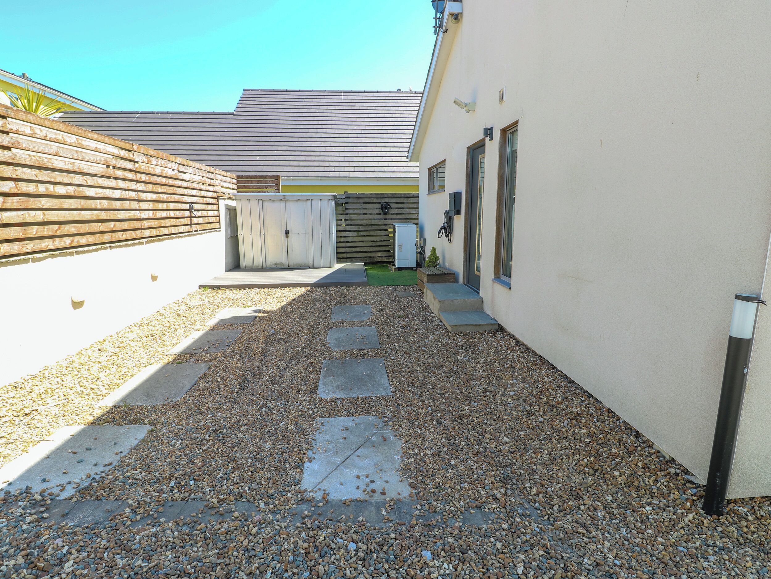 A narrow gravel pathway leading to a building with a wooden fence on one side and a garage on the other.