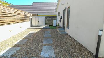 A narrow gravel pathway leading to a building with a wooden fence on one side and a garage on the other.