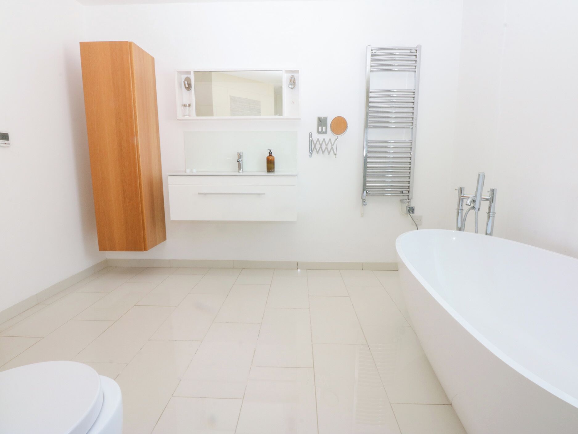Ein modernes Badezimmer mit einem weißen Waschtisch, einer freistehenden Badewanne und einem Holzkabinet.