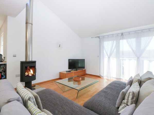 Una sala de estar moderna con una estufa de leña, una mesa de centro de vidrio, un sofá y una televisión.