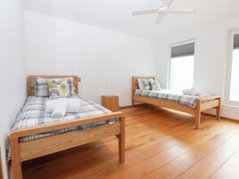 A room with two wooden beds, white walls, and a large window.