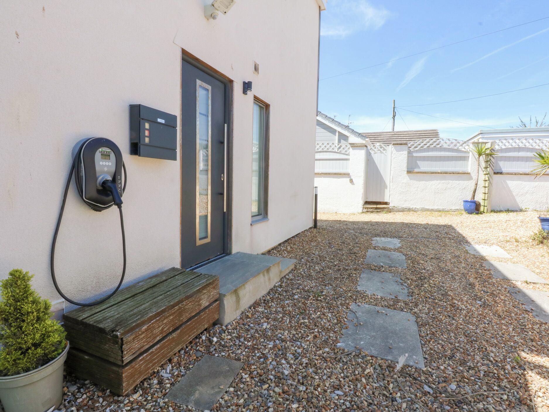A building with a charging station, a door, and a small garden area with gravel and stepping stones.