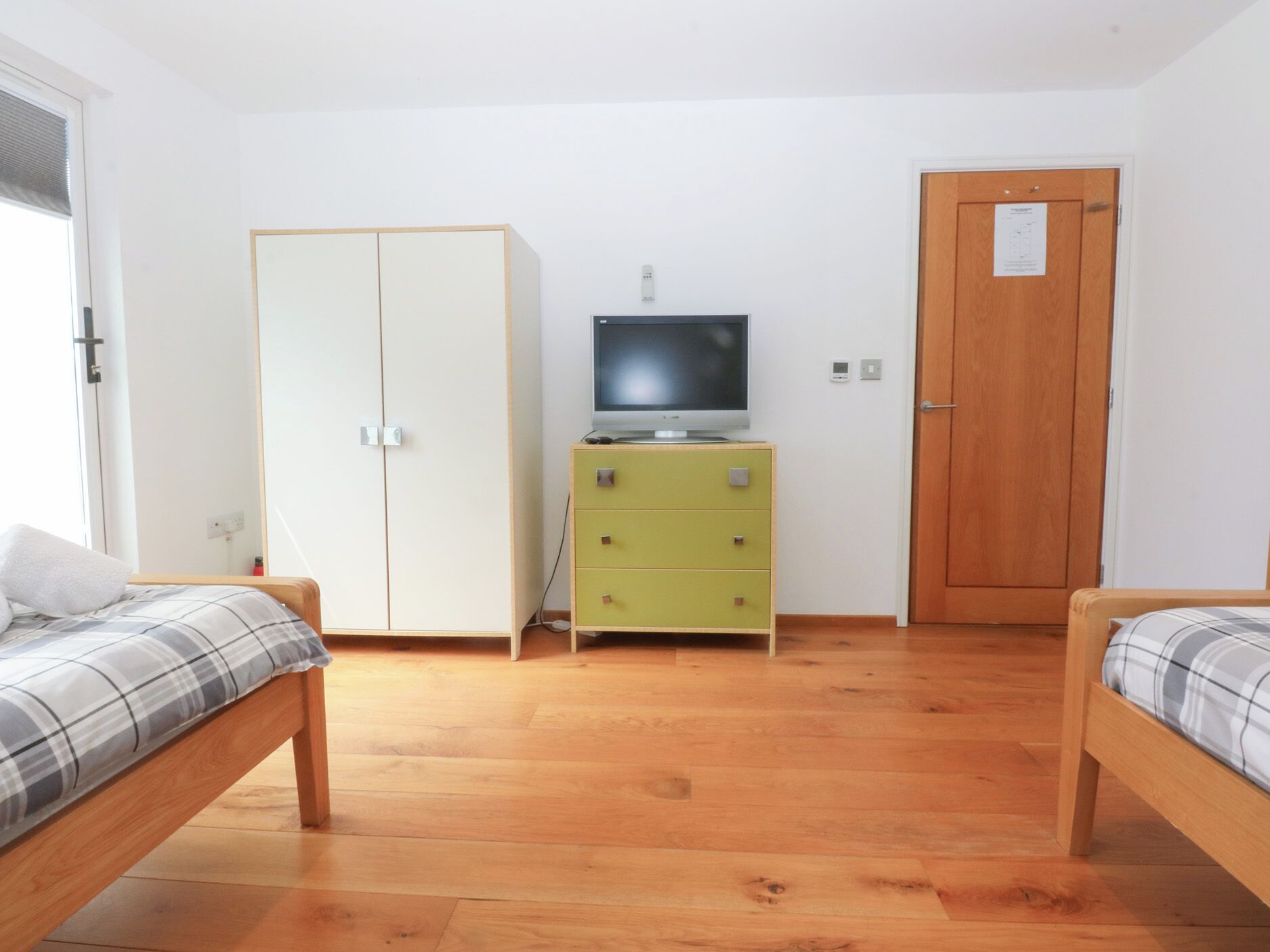 A room with two beds, a wardrobe, a television on a stand, and a wooden door.