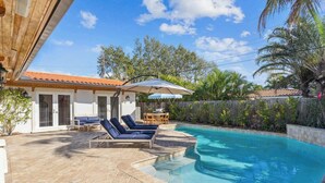 Une piscine dotée de chaises longues et d’un parasol, entourée d’une terrasse et d’une clôture en bois.