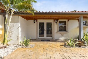 A building with a tiled entrance, a wooden pergola, and a palm tree.
