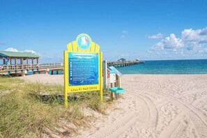 A beach with a lifeguard sign, a pier, and a lifeguard tower.