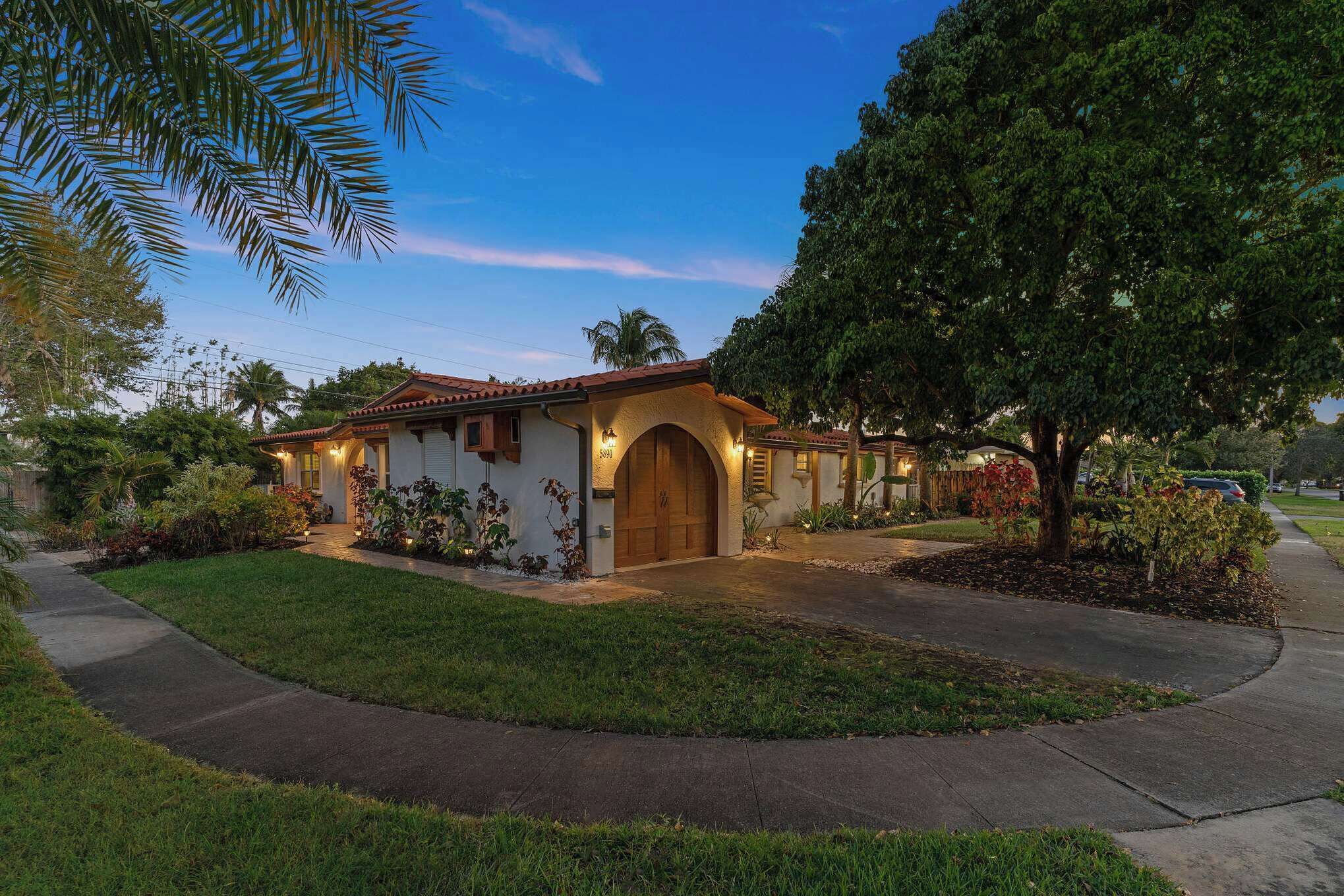 A residential property with a well-maintained lawn, a paved driveway, and a large tree in the front yard.