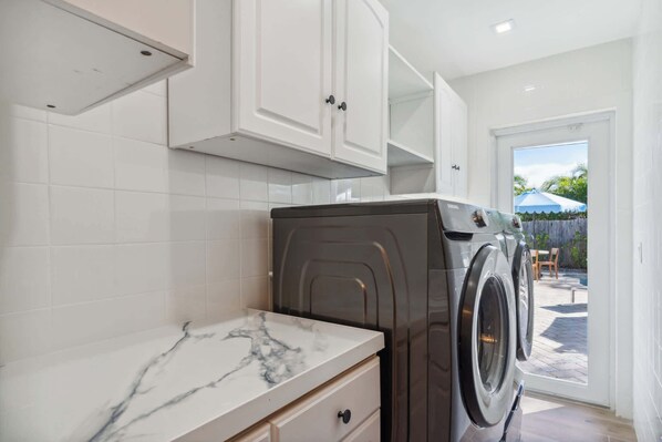 A laundry room with a washing machine, a marble countertop, and white cabinets.
