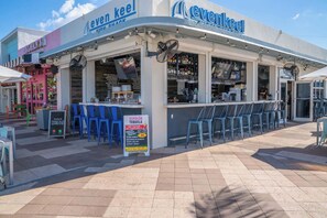 A waterfront restaurant with outdoor seating and a sign advertising cocktails.