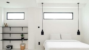A modern bedroom with a bed, two wall-mounted shelves, a small potted plant, a waste bin, and a picture frame.