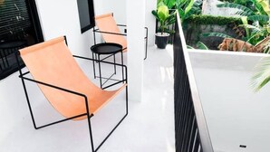 A modern room with a black metal chair and a small round table. There is a potted plant on the windowsill and a balcony with a view of greenery.
