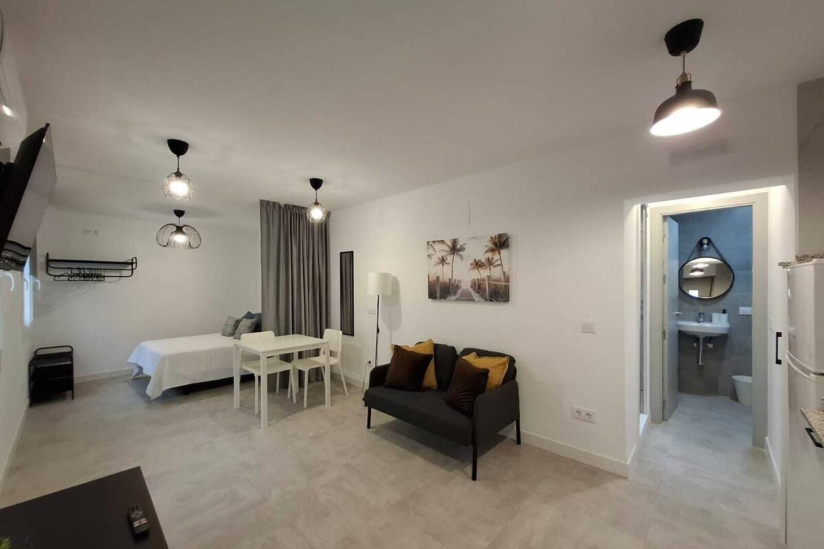 A modern apartment with a dining area, a sofa, a bed, and a bathroom.
