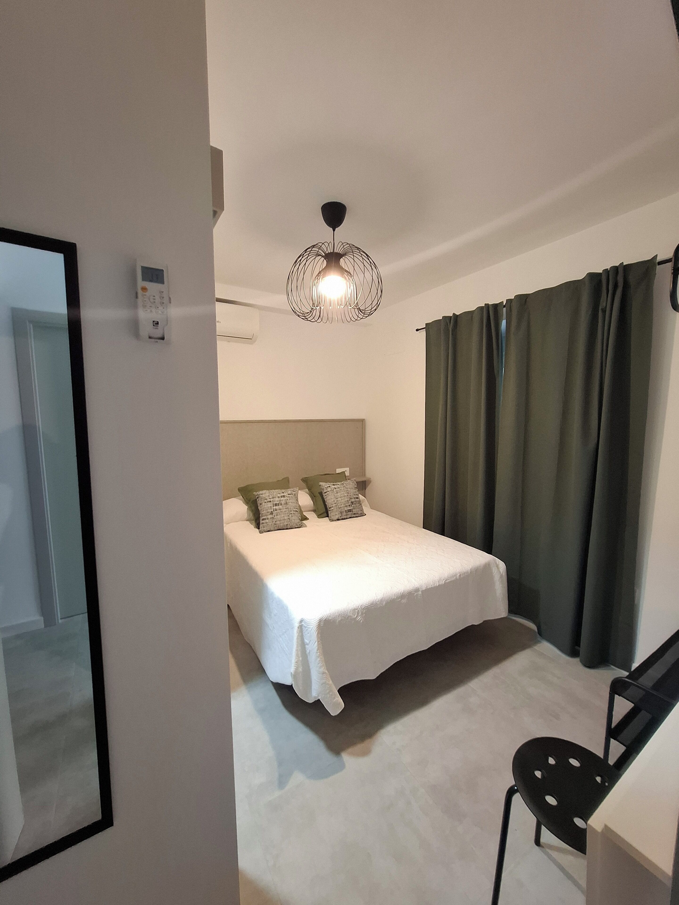 A bedroom with a bed, a chair, a hanging light fixture, and a window with curtains.