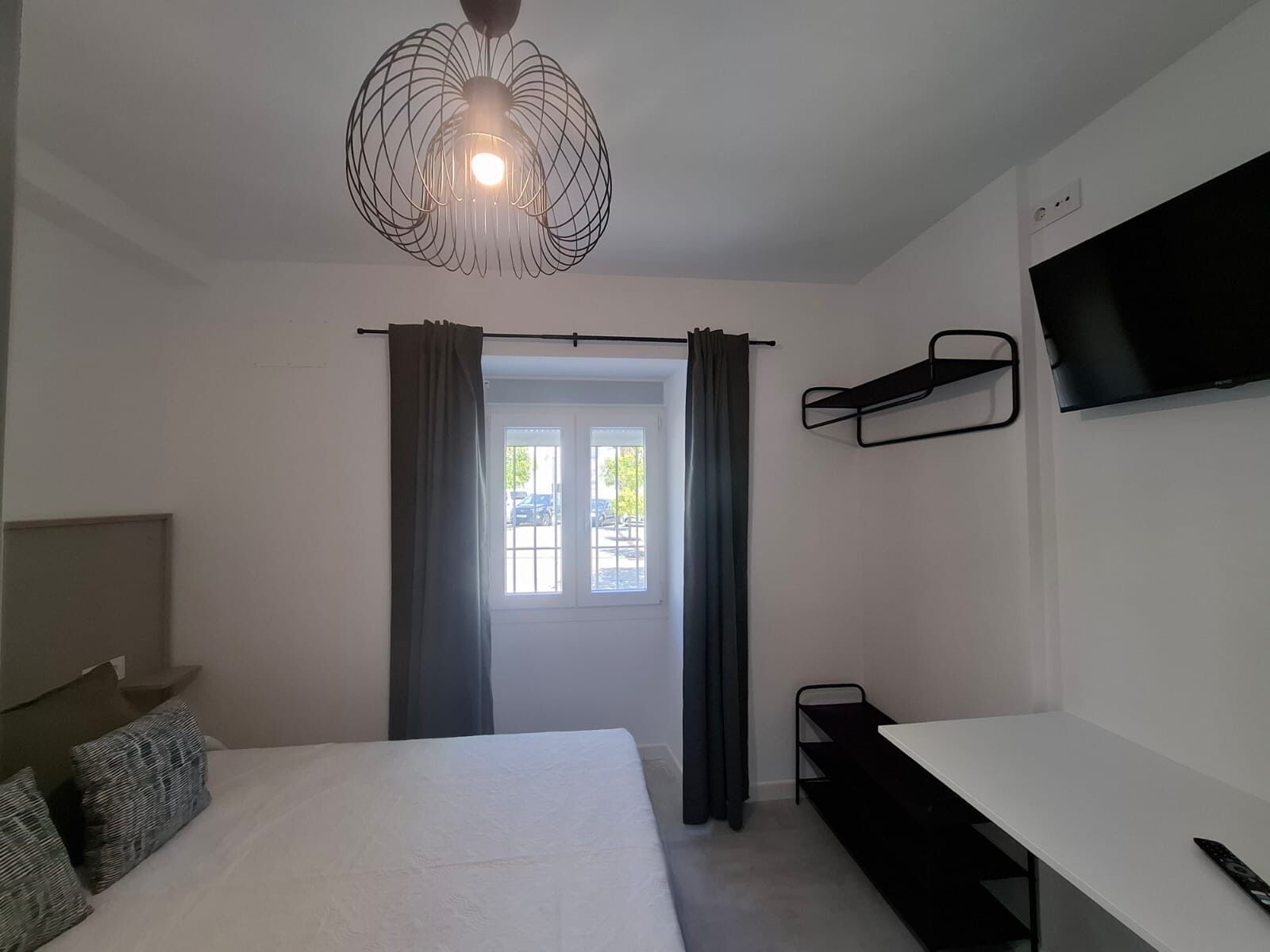 Ett modernt hotellrum med en säng, ett skrivbord, en tv som är monterad på väggen och ett fönster med gardiner.