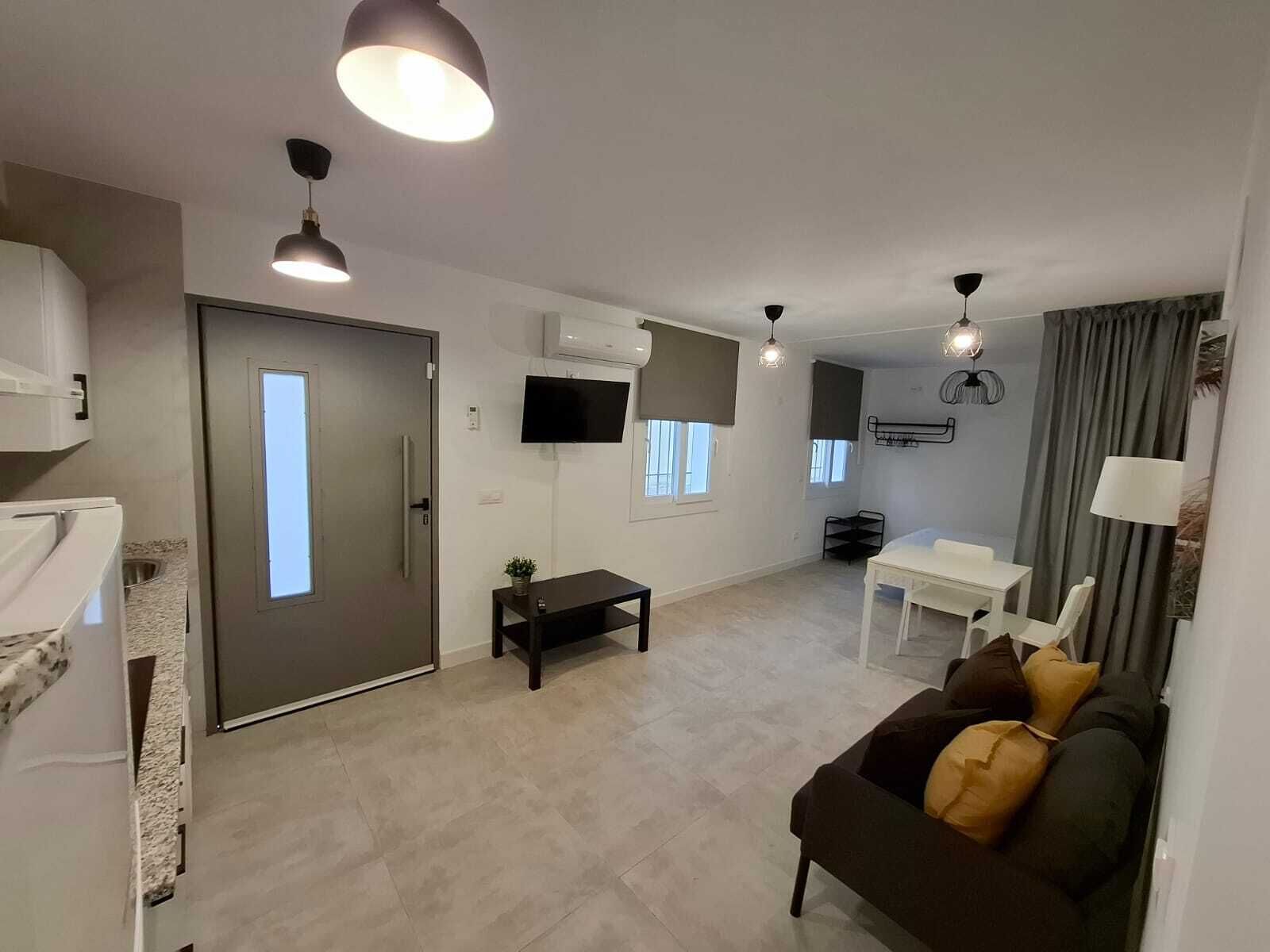 A modern living room with a sofa, a dining table, and a TV mounted on the wall.
