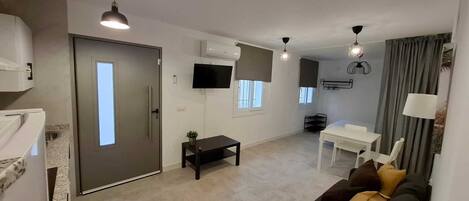 A modern living room with a sofa, a dining table, and a TV mounted on the wall.