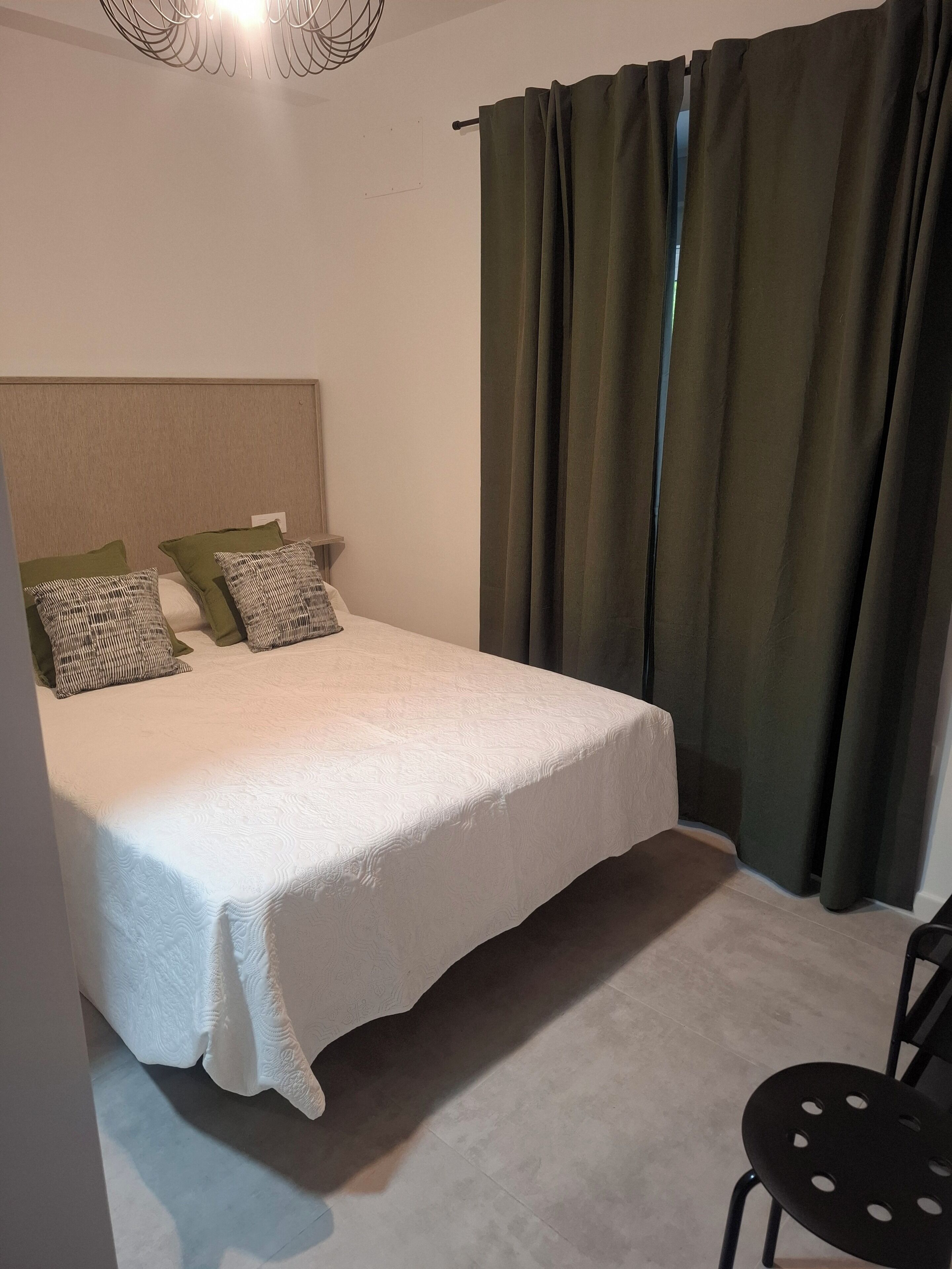 Un dormitorio con una cama, dos almohadas, una silla y una cortina.