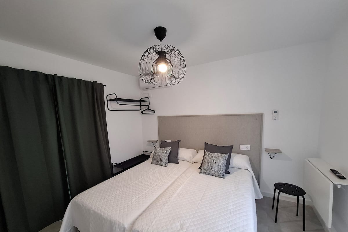 A modern hotel room with a large bed, bedside tables, a desk, and a hanging light fixture.