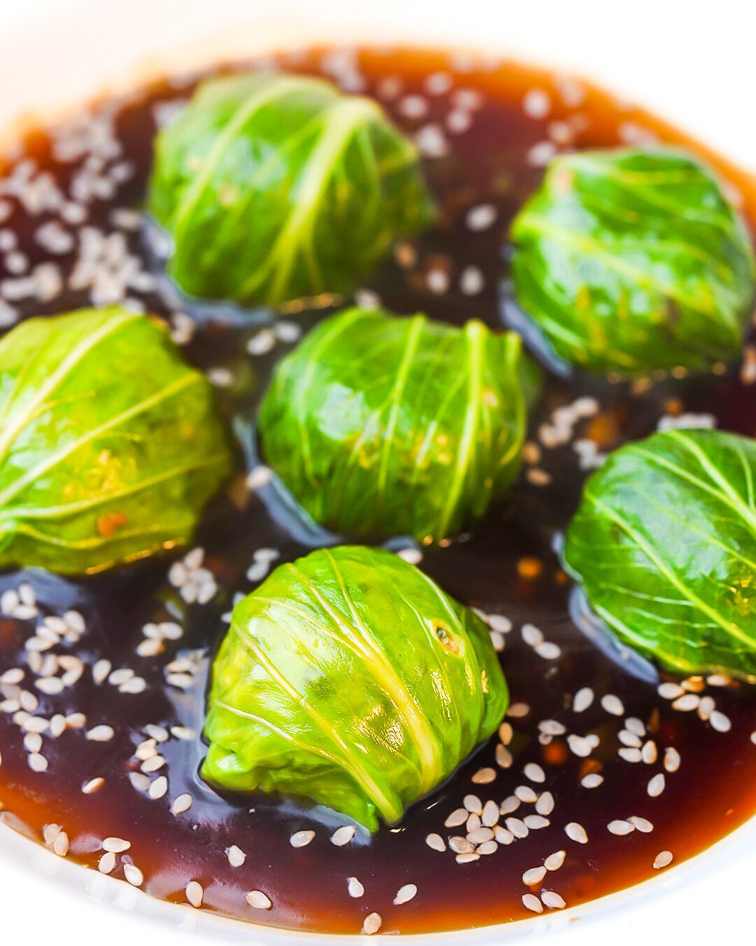 A bowl of cabbage rolls in a dark sauce with sesame seeds.