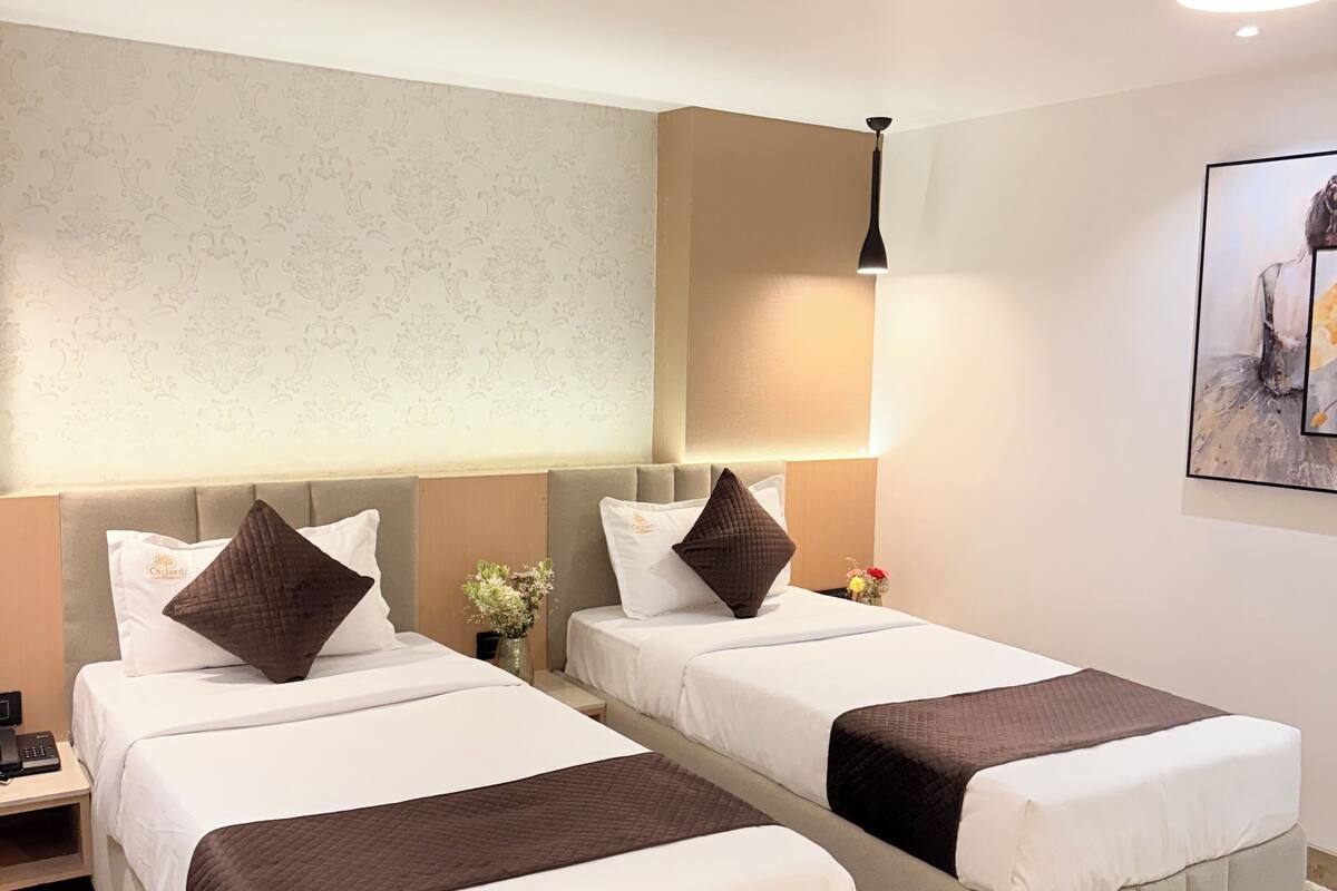Habitación de hotel con dos camas, una mesita de noche, una lámpara y un cuadro en la pared.