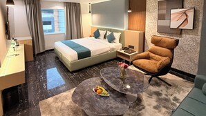 Una habitación de hotel moderna con una cama grande, una zona de estar con una mesita de café, un sofá, un escritorio y un baño.