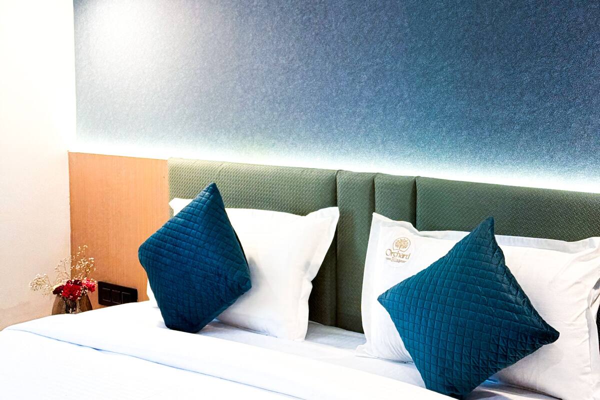 Una habitación de hotel con una cama grande, un cabecero tapizado en verde y una lámpara de pared.