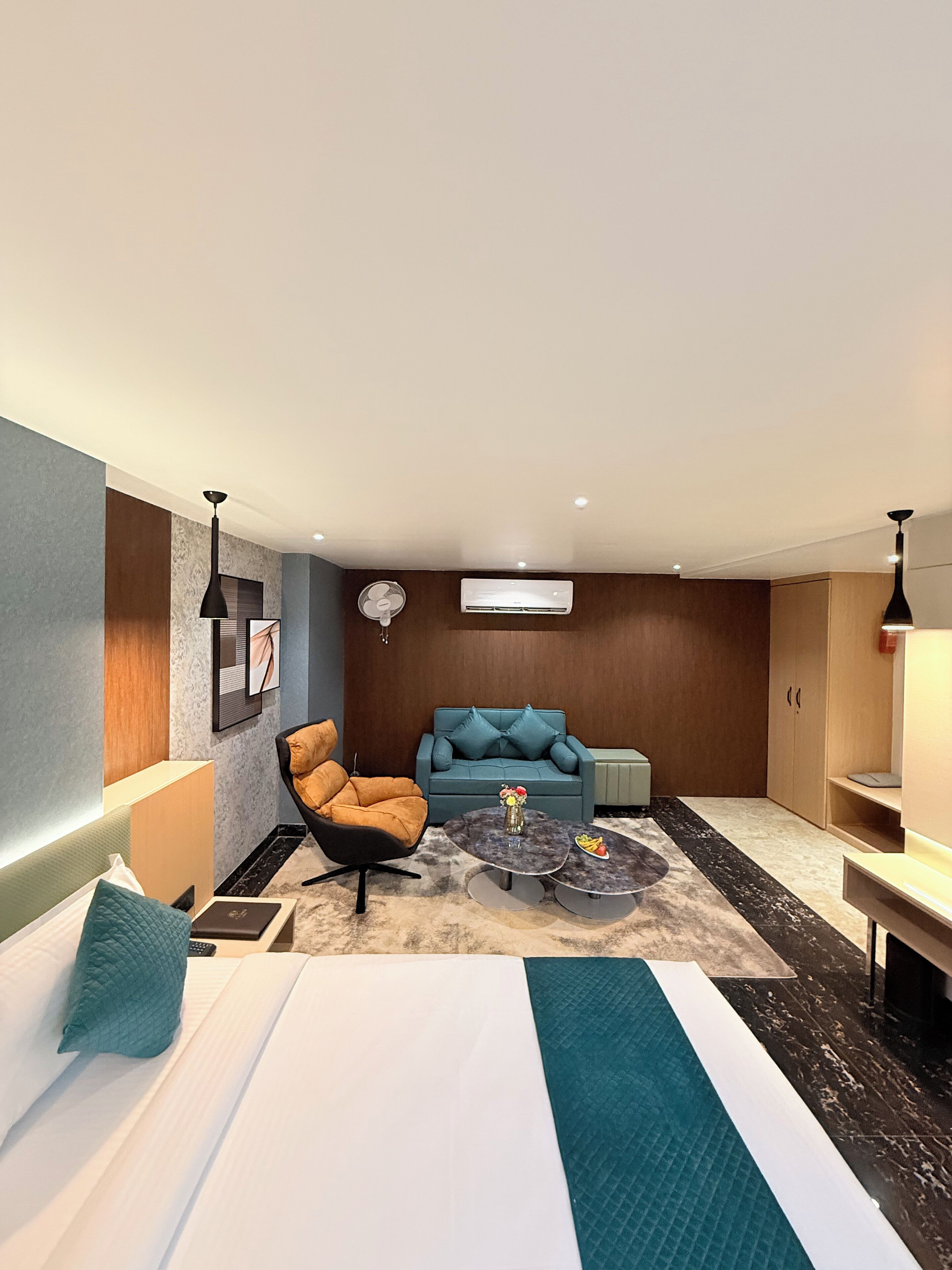 A modern hotel room with a bed, a sofa, a coffee table, and a TV.
