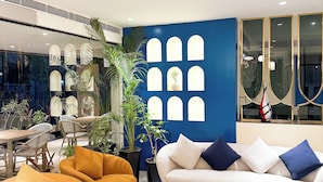 Una sala de estar moderna con una pared azul de acento, un sofá blanco con cojines azules, una mesa de centro redonda y sillones naranjas.