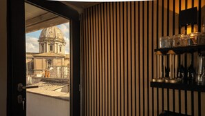 Une pièce avec vue sur un bâtiment historique, visible à travers une fenêtre, un mur fait de lattes de bois et une étagère où sont exposés des objets en verre.