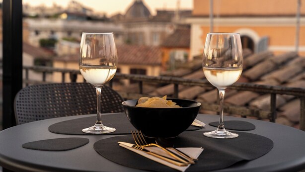Une table avec deux verres à vin, un bol de chips et des couverts, sur un balcon donnant sur un paysage urbain.