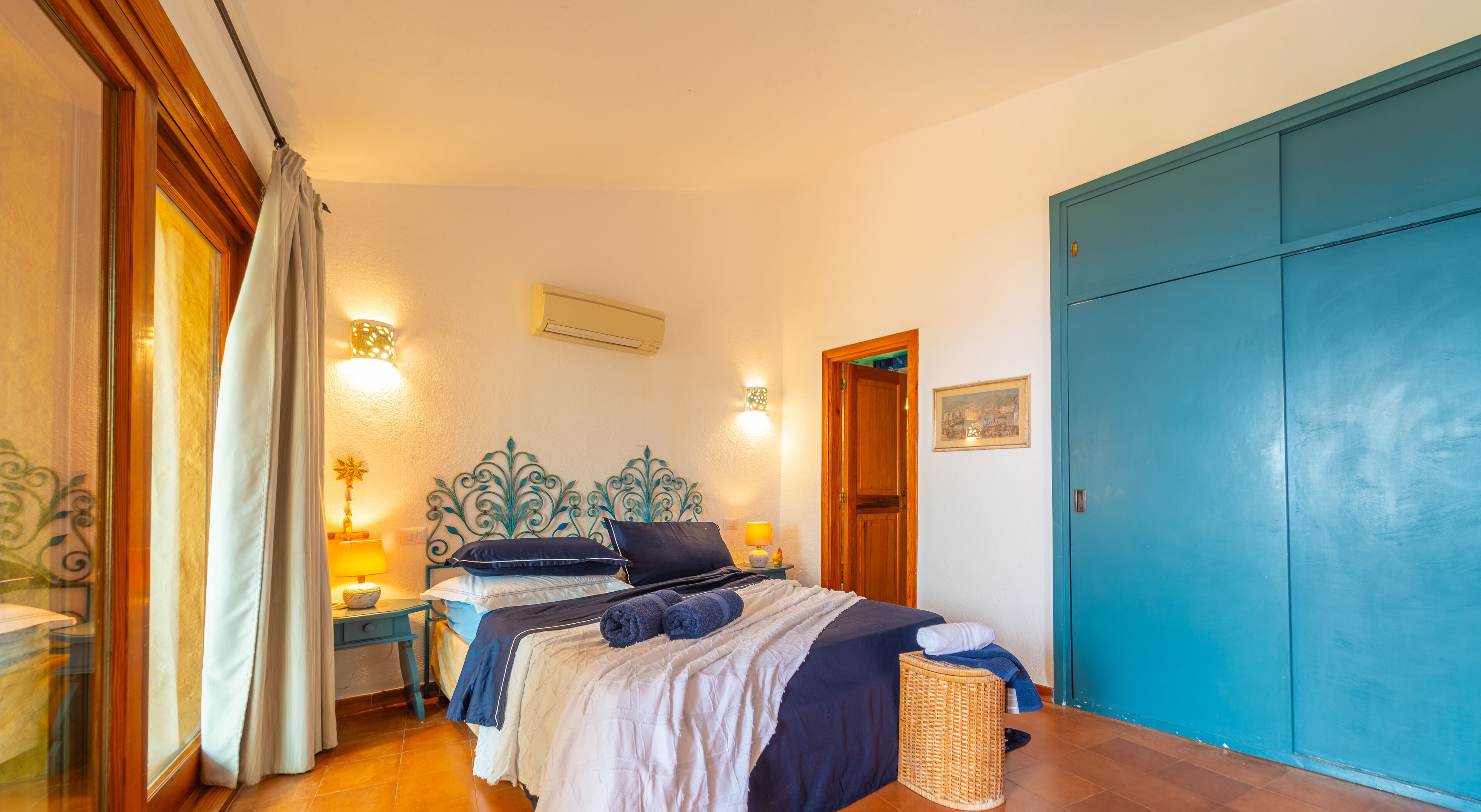 A bedroom with a bed, bedside tables, a lamp, a blue wardrobe, and a door.