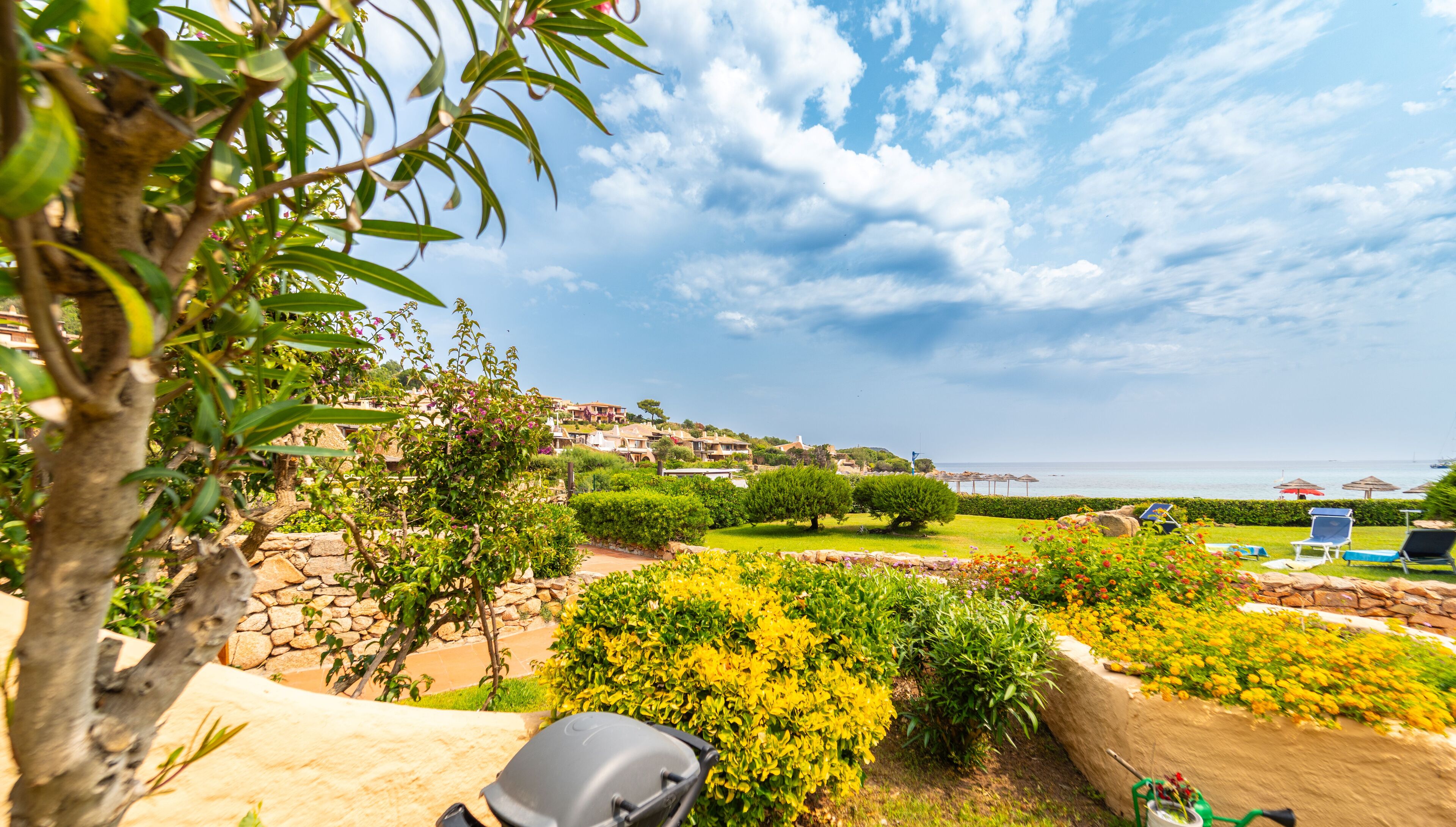 Un jardín ajardinado con vistas al mar, muros de piedra y un césped con flores de colores.