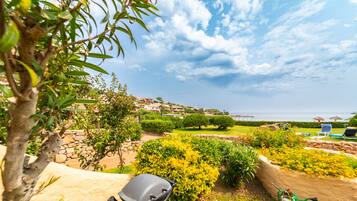 Un jardín ajardinado con vistas al mar, muros de piedra y un césped con flores de colores.