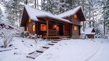 Een vakantiehuisje van hout met een veranda, omringd door met sneeuw bedekte bomen.