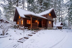 A log cabin with a porch, surrounded by snow-covered trees.