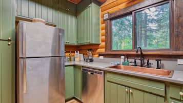 A compact kitchen with green cabinets, a stainless steel refrigerator, and a copper sink.