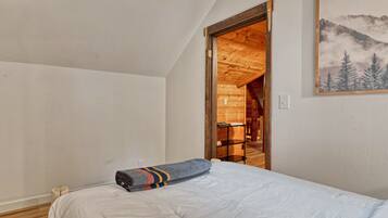 A bedroom with a bed, a wooden door leading to a wooden room, and a mountain landscape painting on the wall.