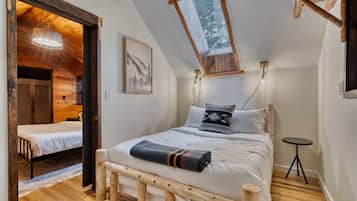 Een slaapkamer met een houten bedframe, een klein nachtkastje, een wandlamp en een raam met uitzicht op bomen.