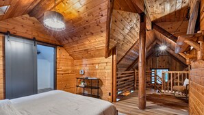 L’intérieur d’une cabane en bois, avec un lit, une table et un escalier menant à un niveau supérieur.
