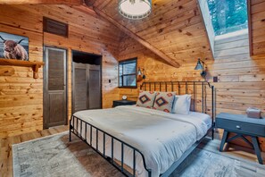 Ein Schlafzimmer in einer Holzhütte mit einem Bett, Nachttisch, Lampe und einer Uhr.